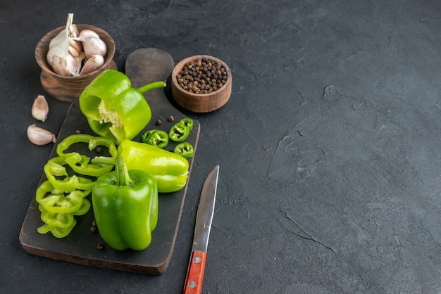 Vue rapprochée de poivrons verts coupés entiers coupés sur une planche à découper en bois de couleur foncée sur le côté droit sur une surface noire