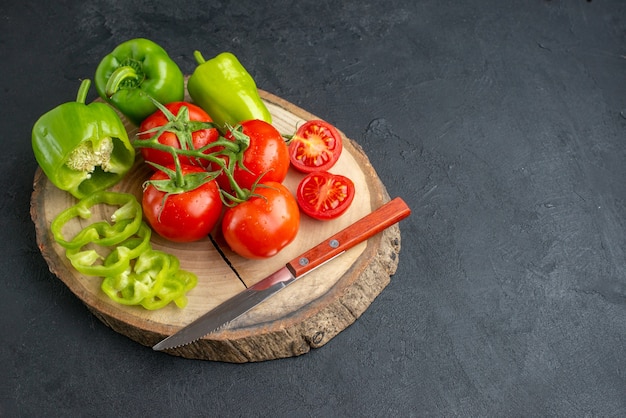 Vue rapprochée de poivrons verts coupés entiers et de tomates fraîches couteau sur une planche à découper en bois sur le côté droit sur une surface noire