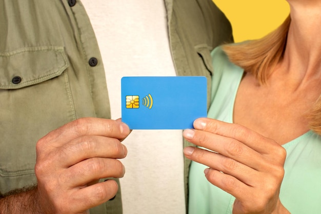Vue rapprochée recadrée d'un couple d'âge moyen méconnaissable tenant une carte de crédit faisant la promotion du sans contact