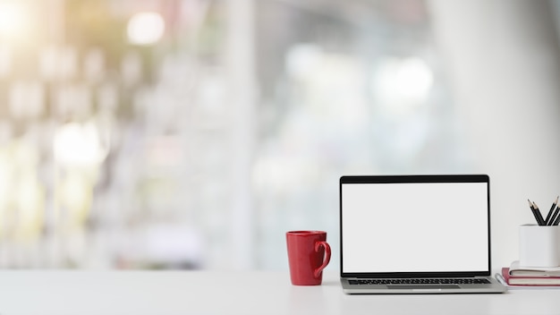 Vue rapprochée de la salle de bureau avec ordinateur portable à écran blanc, papeterie, tasse à café et espace copie sur tableau blanc