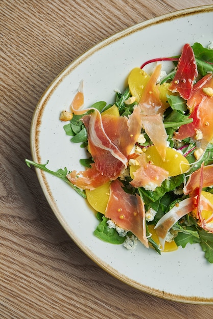 Photo vue rapprochée sur une savoureuse salade légère au prosciutto, un mélange de légumes verts, d'ananas et de fromage bleu dans un élégant bol gris.