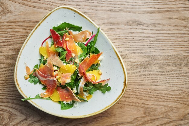 Vue rapprochée sur une savoureuse salade légère au prosciutto, un mélange de légumes verts, d'ananas et de fromage bleu dans un élégant bol gris.