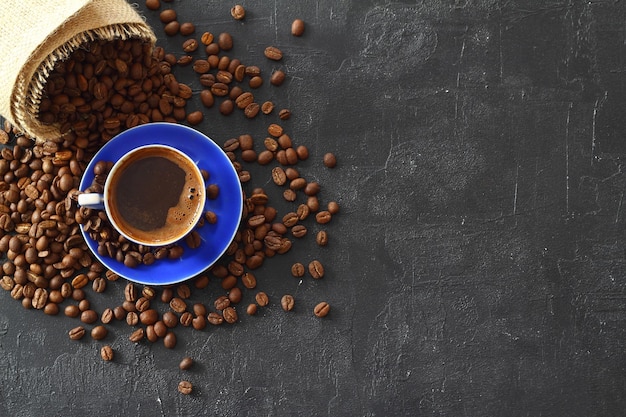 Vue rapprochée et supérieure du café noir chaud dans une tasse de café bleue et des grains de café thaïlandais rôtis sur du bois