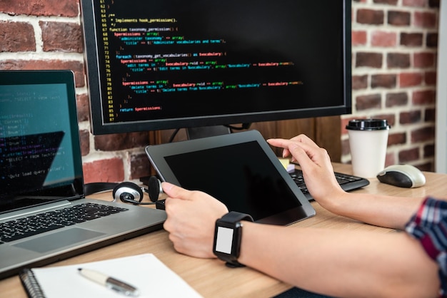 Photo la vue rapprochée de l'utilisation de la tablette sur le bureau avec d'autres services électroniques autour par une programmeuse.