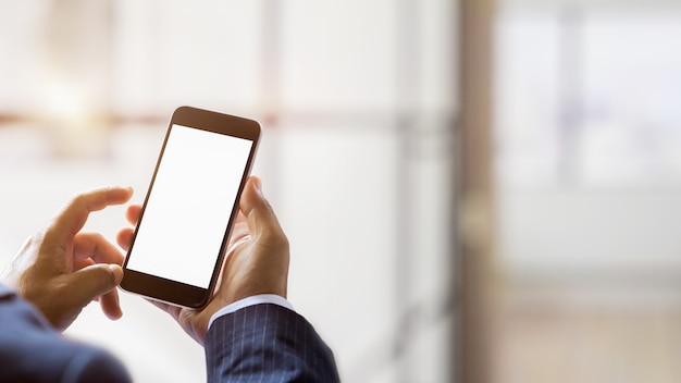 Vue rapprochée de l'utilisation d'un téléphone à écran blanc avec l'arrière-plan flou de la salle de bureau