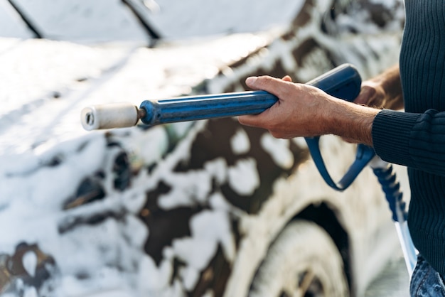 Vue recadrée du jeune homme caucasien tenant un pistolet à haute pression tout en se préparant à pulvériser sur sa voiture pendant le nettoyage. Stock photo