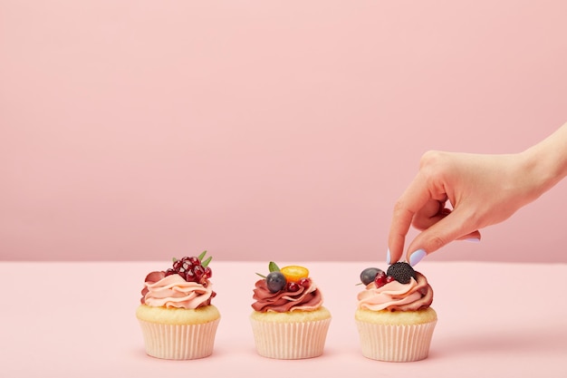 Vue recadrée de la femme avec des cupcakes sucrés avec des fruits et des baies isolés sur rose