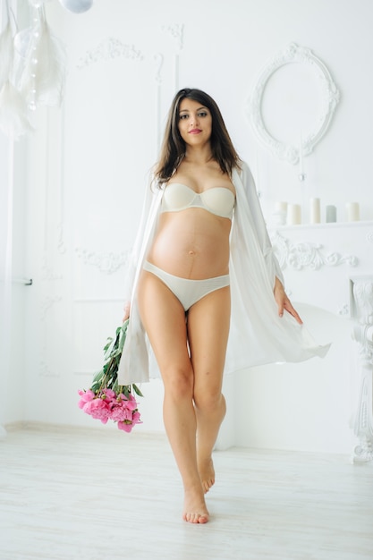 Vue recadrée de femme enceinte posant en sous-vêtements blancs, isolé sur blanc