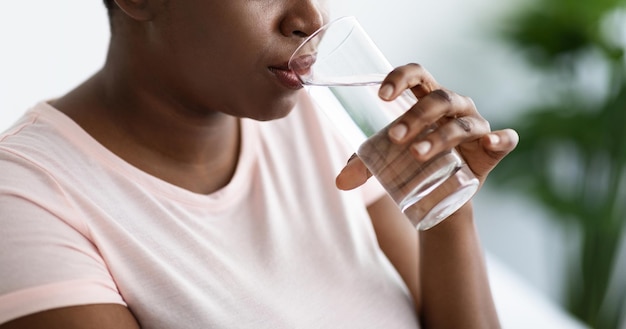 Photo vue recadrée d'une femme noire en surpoids buvant de l'eau minérale à partir d'un panorama en verre à l'intérieur