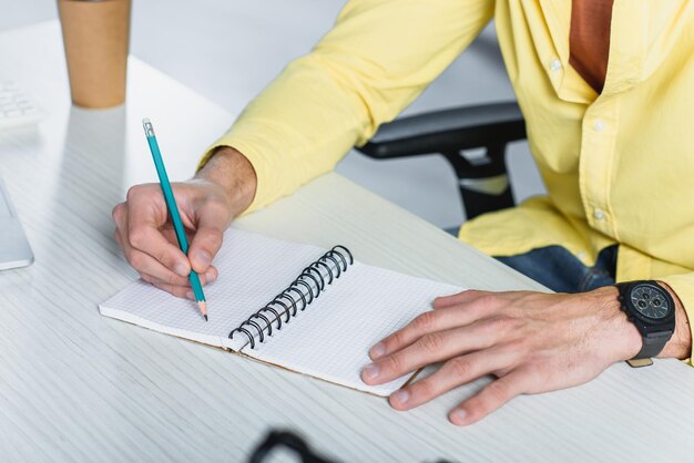 Vue recadrée de l'homme écrivant dans un cahier au bureau