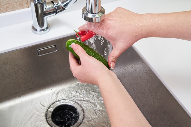 Vue recadrée de mains féminines éplucher le concombre sur un broyeur de déchets alimentaires dans un évier dans une cuisine moderne