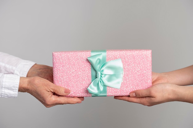 Vue recadrée des mains de la jeune femme donnant un cadeau dans un emballage rose avec un arc à une femme âgée isolée sur fond blanc Concept de la fête des mères