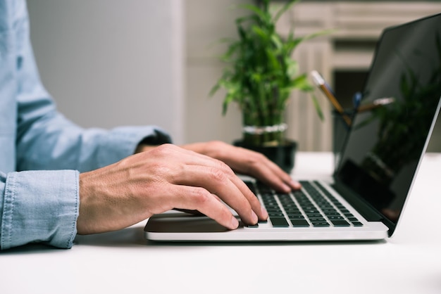 Vue recadrée des mains masculines tapant sur un ordinateur portable sur le lieu de travail