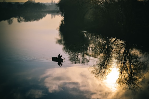 Vue sur la rivière un pêcheur de silhouette en bateau naviguant