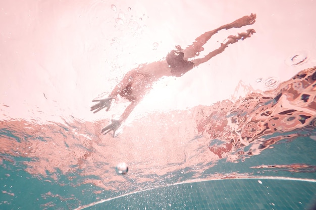 Vue sous-marine du corps entier d'un homme irréconnaissable en short de natation nageant dans l'eau propre et transparente de la piscine