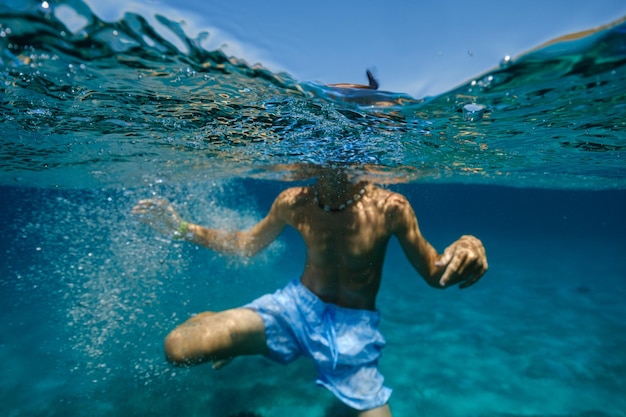 Vue sous-marine d'un garçon torse nu anonyme en short plongeant dans l'eau de mer bleue pendant les vacances d'été