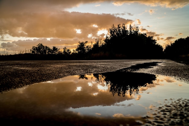 Vue spectaculaire d'une route mouillée et reflet d'un ciel au coucher du soleil après la tempête dans une flaque