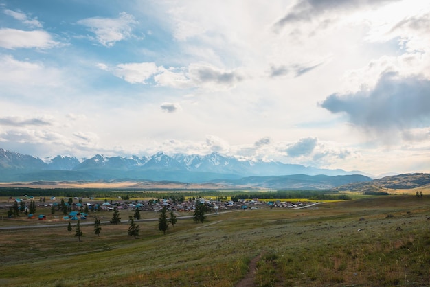 Photo vue spectaculaire sur le village de montagne et les montagnes enneigées sous un ciel nuageux paysage alpin avec village et haute chaîne de montagnes enneigées sous les nuages par temps changeant ensoleillé et couvert en même temps