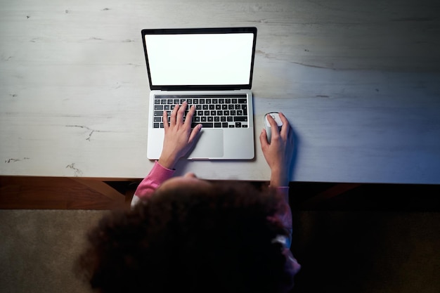 Vue supérieure femme afro inconnaissable assise à une table ou à un bureau dans une pièce utilisant un papier peint blanc pour ordinateur portable