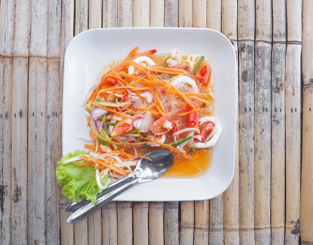 Photo vue supérieure des fruits de mer salade de nouilles en verre sur une assiette blanche sur une table en bois de bambou nourriture thaïlandaise épicée