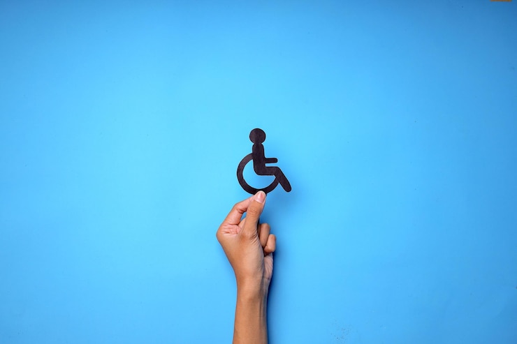 Photo vue supérieure d'un handicapé tenant la main avec un fauteuil roulant coupé en papier isolé sur fond bleu