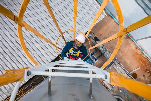 Vue supérieure ouvrier masculin descend l'échelle inspection réservoir inoxydable travail en hauteur harnais de sécurité