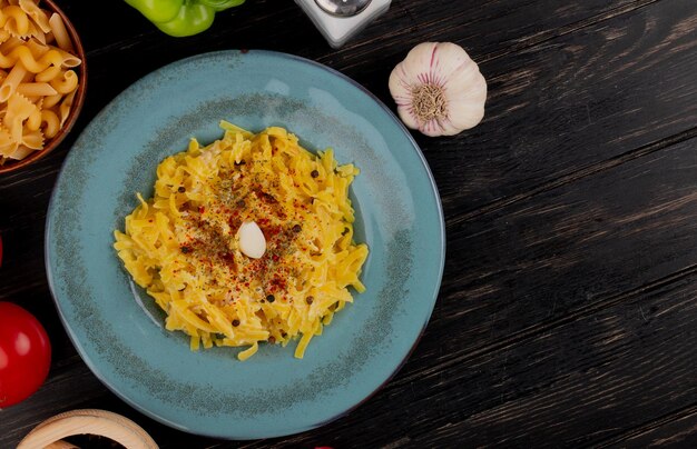 vue supérieure de pâtes de macaroni dans une assiette avec du sel, de l'ail et du sel de tomate au fond en bois avec un espace de copie