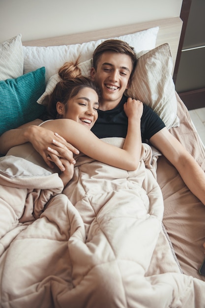 Vue supérieure photo d'un couple caucasien allongé dans son lit recouvert d'une couverture souriant et embrassant
