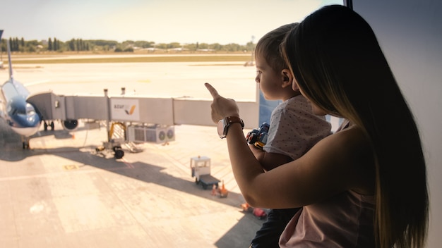 Vue tonique de la jeune mère montrant des avions sur la piste à l'aéroport à son petit fils.