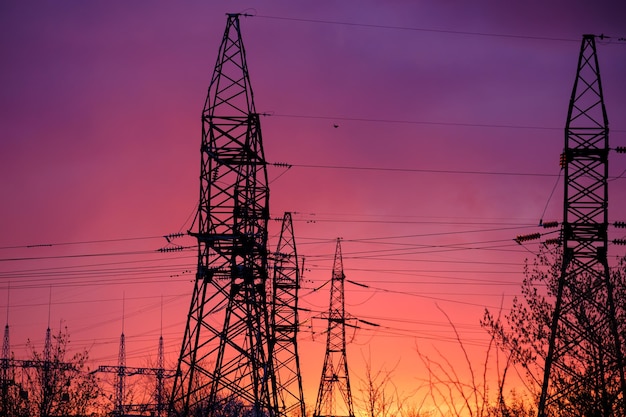 Vue de la tour de transmission de puissance du pôle haute tension sur la tour haute tension panoramique au coucher du soleil avec alimentation