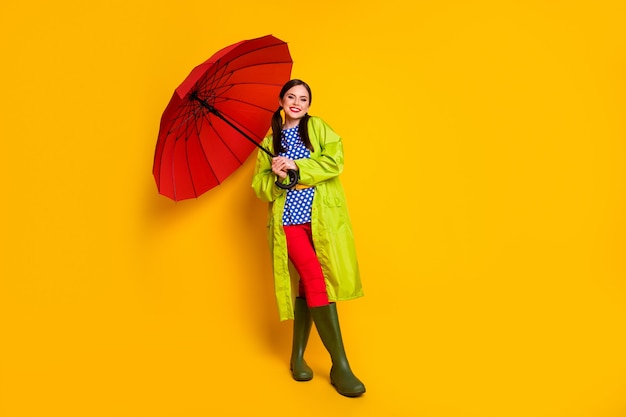 Photo vue sur toute la longueur de la taille du corps d'elle elle jolie jolie fille gaie et gaie portant une cape verte parasol ouvert octobre posant isolé fond de couleur jaune vif éclatant brillant