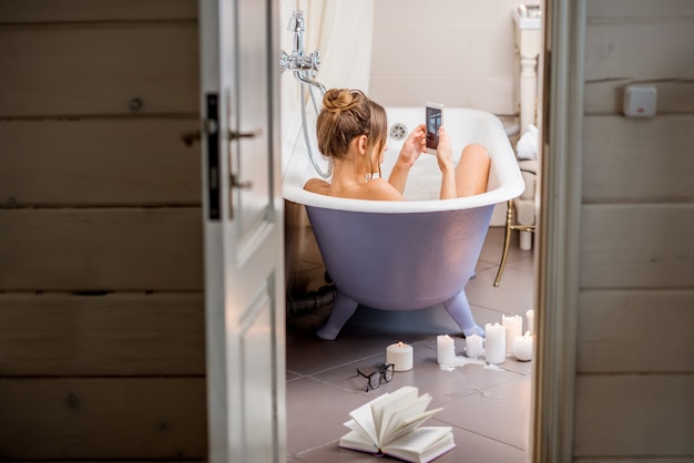 Vue à travers la porte de la salle de bain sur la belle femme se relaxant dans la baignoire rétro