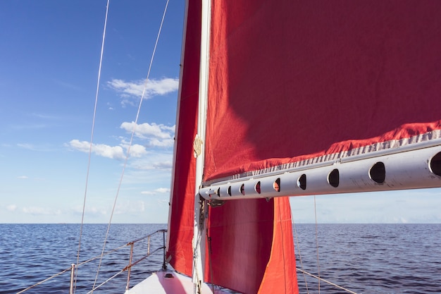 Vue vers l'avant depuis le cockpit d'un yacht aux voiles rouges, naviguant le long de la mer jusqu'à l'horizon