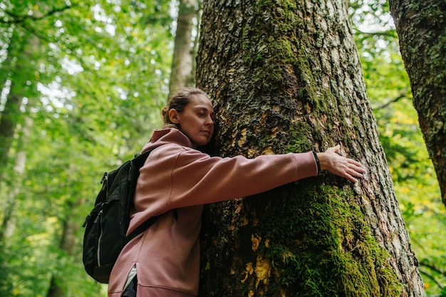 Vue vers le haut d'une jeune femme serrant un arbre de mousse épaisse dans une forêt