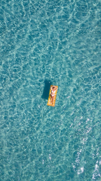 Vue verticale aérienne de la femme se détendre et profiter des vacances d'été portant sur un matelas lilo gonflable coloré sur la surface de l'eau bleue Personnes appréciant la destination de voyage océan Vertical