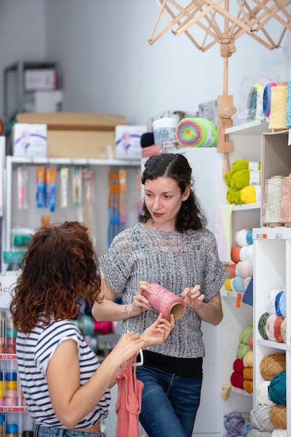 Vue verticale de l'aide assistant sur un magasin de détail aidant une femme à acheter une pelote de laine rose