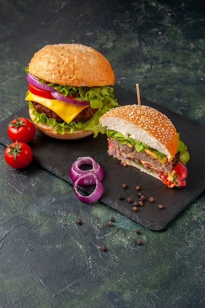 Vue verticale de la coupe de délicieux sandwichs et tomates avec des oignons sur plateau noir sur une surface sombre