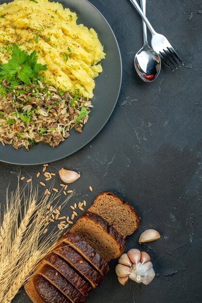 Vue verticale d'un délicieux dîner avec de la viande et de la purée de pommes de terre sur une assiette grise tranches de pain couverts à l'ail sur fond noir