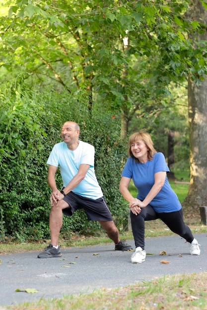Vue verticale de deux adultes souriant et s'amusant tout en faisant de l'exercice dans le parc avec un environnement naturel autour