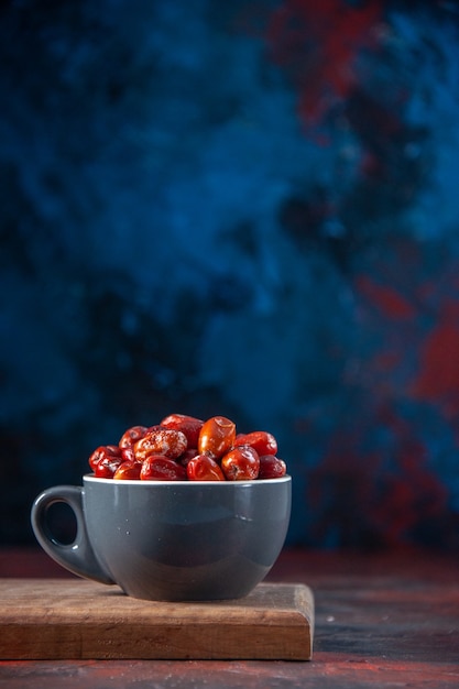 Vue verticale des fruits crus frais de silverberry dans une tasse de couleur grise sur planche de bois sur le côté droit sur fond de couleurs mélangées