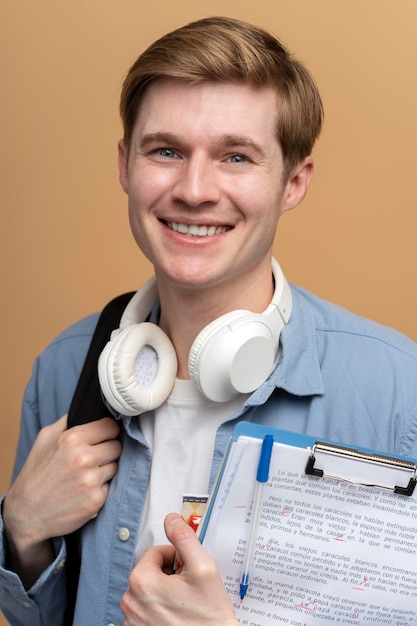 Vue verticale d'un jeune étudiant souriant avec des livres et un sac à dos en regardant la caméra