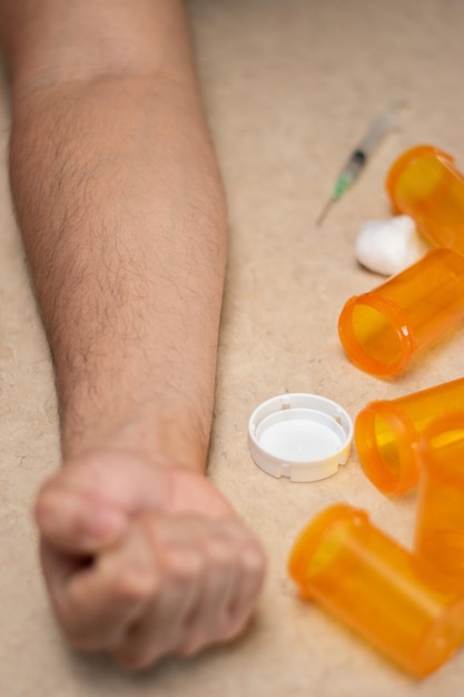 Vue verticale de la main d'une personne dans une table avec une seringue et des bouteilles vides de concept de toxicomane