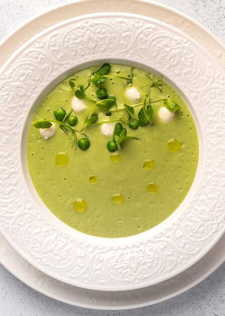 Vue verticale de la purée de soupe maison de pois verts, lait de coco avec mini fromage mozzarella en blanc