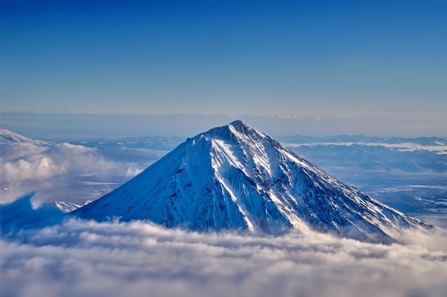 Vue sur le volcan enneigé depuis l'illuminateur de l'avion Haut volcan endormi au-dessus des nuages