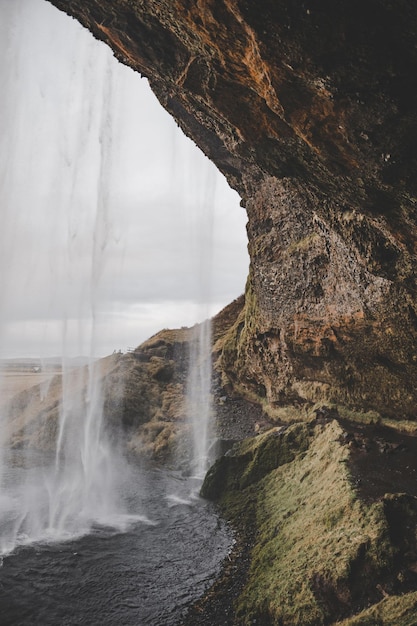 Vues depuis l'intérieur d'une cascade en Islande sur une formation rocheuse et un paysage en arrière-plan