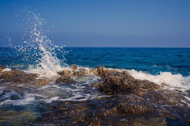 Vues magnifiques sur la mer Méditerranée bleue Roches ensoleillées vagues avec de la mousse et des éclaboussures d'eau La vague s'écrase sur les rochers sur le rivage