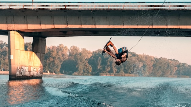 En wakeboard, le wakeboarder fait le tour du backflip sur la rivière sous le pont. Heure du matin