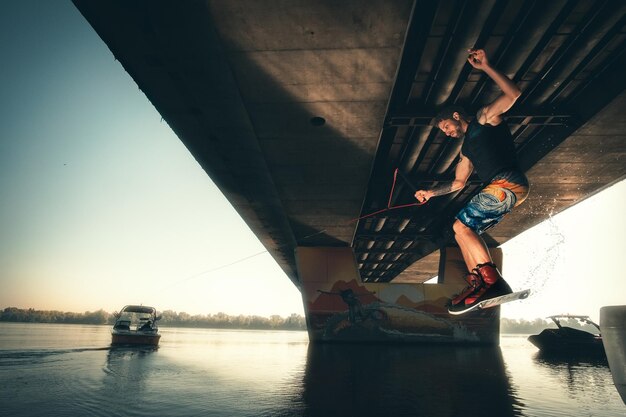 Wakeboard, wakeboarder sautant derrière le bateau avec wakeboard, action sous le pont