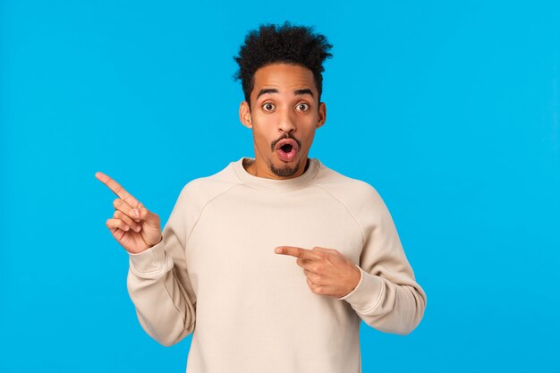 Waouh incroyable. Impressionné et étonné, afro-américain sans voix avec coupe de cheveux afro, gars hipster pointant dans le coin supérieur gauche, lèvres pliantes et haletant d'un événement impressionnant à couper le souffle