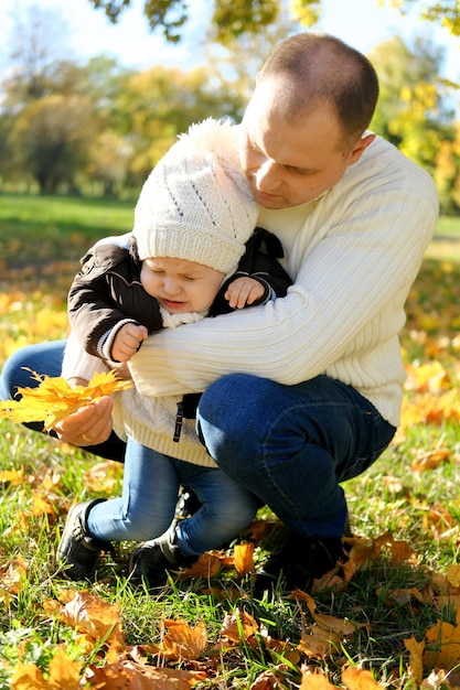 Photo week-end familial dans le parc d'automne le père montre au petit fils des feuilles jaunes mais le bébé est méchant